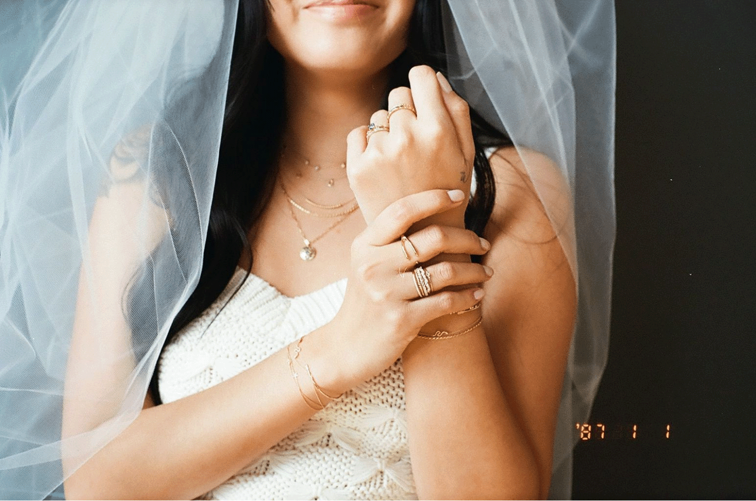 A close-up of a girl wearing a veil. She is showing off all the gold jewelry she is wearing. Shot on 35mm film.
