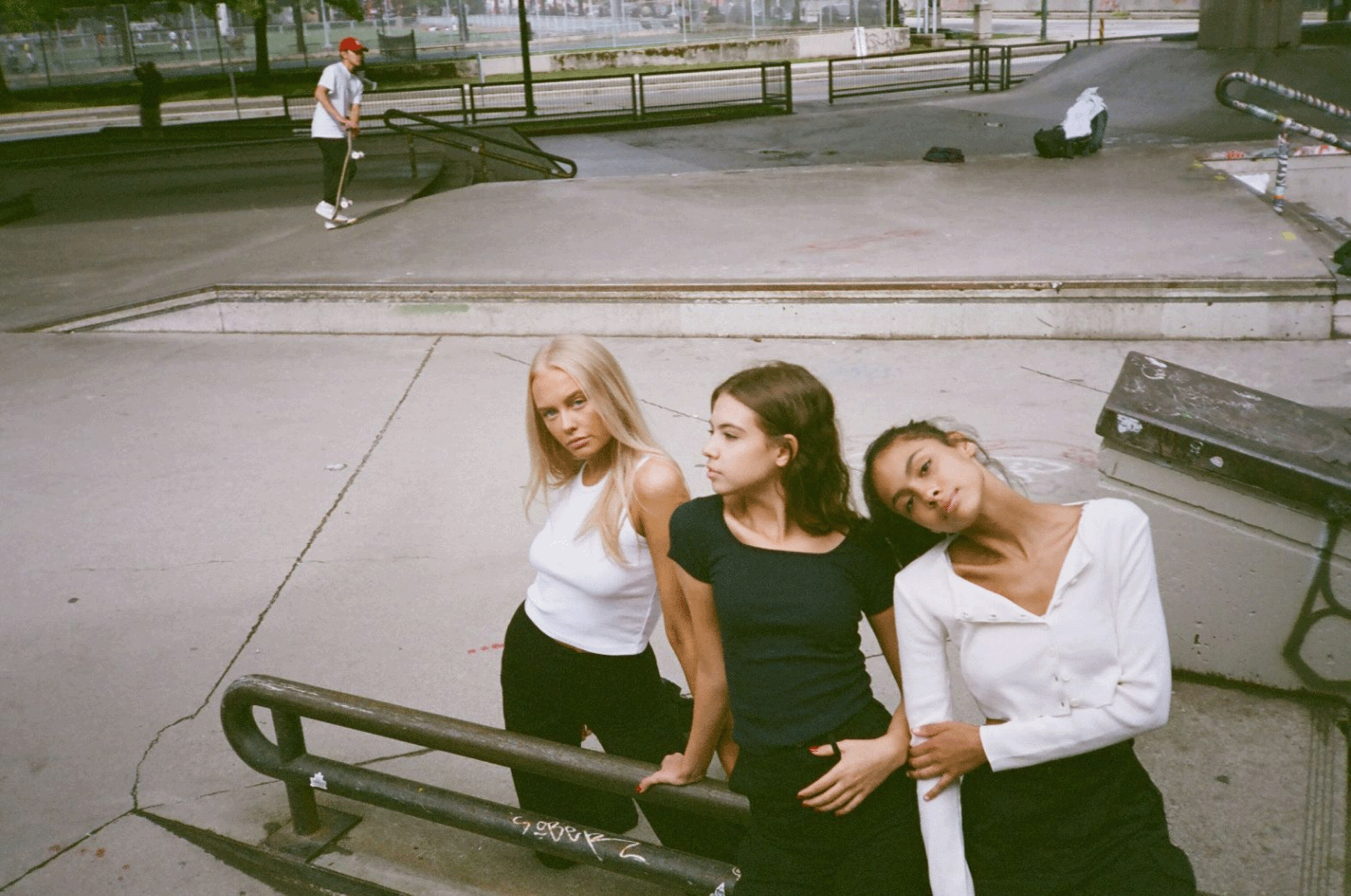 Three girls hanging out in a skate park with skateboaders in the background. Shot on 35mm film. 