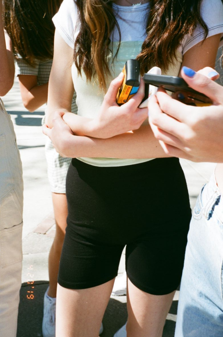 A close-up of a group of girls holding their phones and disposable film cameras. Shot on 35mm film.