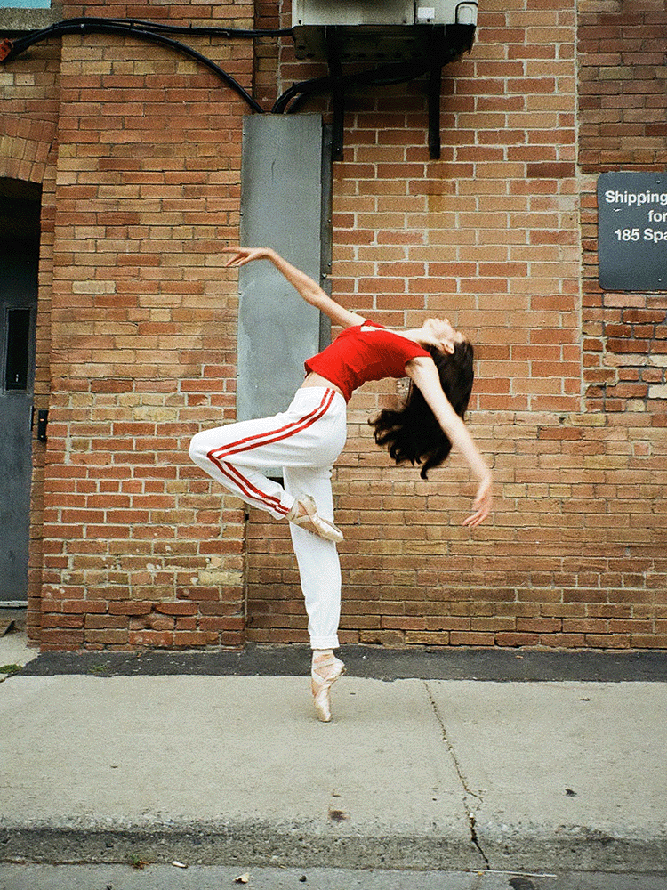 A ballerina dancing on the sidewalk in front of a brick warehouse. Shot on 35mm film.